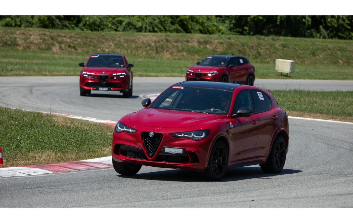 Tre SUV Alfa Romeo rossi percorrono una curva su un circuito da corsa asfaltato.